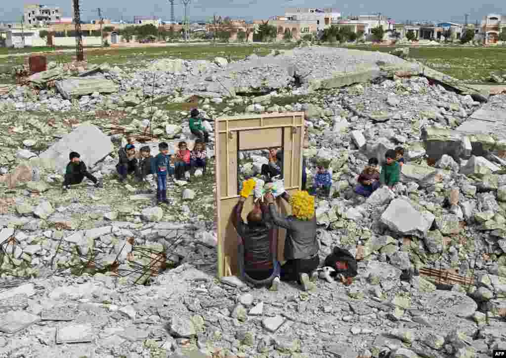 Syrian actor Walid Abu Rashed (yellow wig) and a fellow actor entertain children through a makeshift puppet theatre set up among the rubble of collapsed buildings in the town of Saraqib in the rebel-held northern Idlib province.