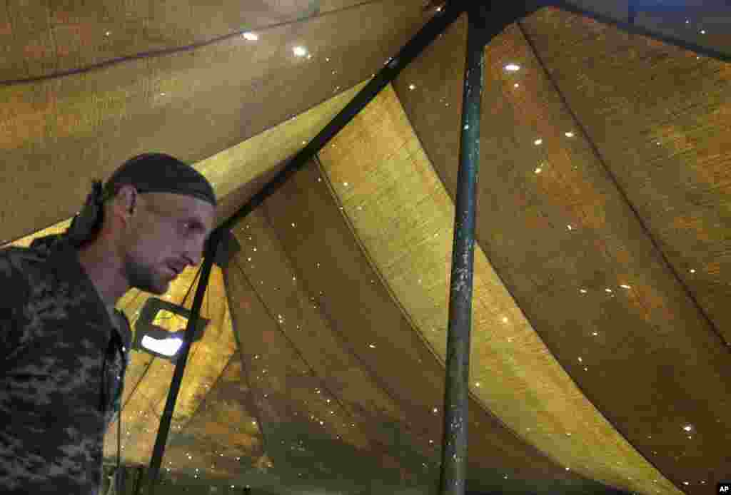 A Pro-Russian rebel stands in a tent riddled with holes caused by shrapnel at the Novoazovsk border crossing point, in eastern Ukraine, Aug. 29, 2014.