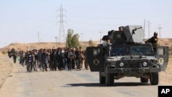 FILE - Elite counterterrorism forces escort people fleeing their homes during clashes between Iraqi security forces and the Islamic State group in Hit, 85 miles (140 kilometers) west of Baghdad, Iraq, April 4, 2016. 