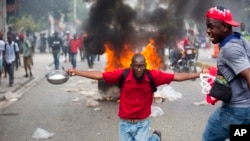 Un manifestante se arrodilla sosteniendo un tazón y una cuchara para mostrar su hambre durante protestas en Haití el jueves.