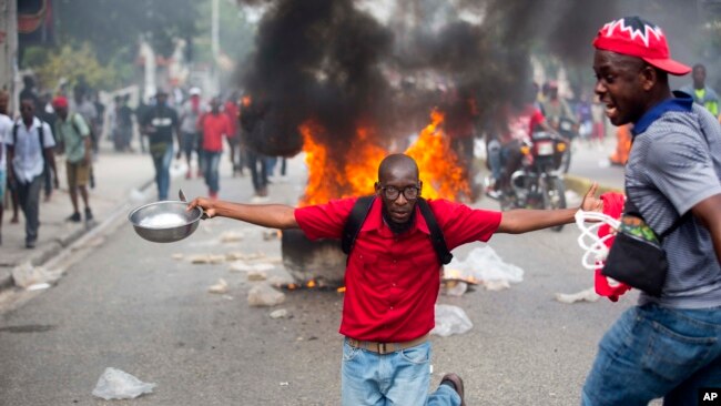 Un manifestante se arrodilla sosteniendo un tazón y una cuchara para mostrar su hambre durante protestas en Haití el jueves.