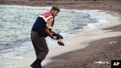 A paramilitary police officer carries the lifeless body of a migrant boy near the Turkish resort of Bodrum early Wednesday, Sept. 2, 2015. (AP Photo/DHA)