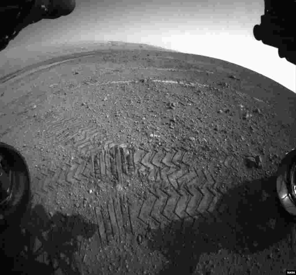 This image shows track marks from the rover's first Martian drives. The rover's Bradbury Landing site and its first tire marks are seen at center, in the distance, while tracks from the second drive are in the foreground. Mount Sharp is on the horizon.