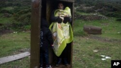 A Syrian woman with her children takes a shelter in a iron box during a rainfall, after they arrived from Turkey to the Greek deserted island of Pasas near Chios on Wednesday, Jan. 20, 2016 .