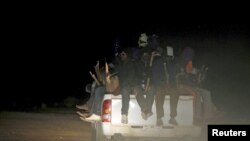 FILE - Migrants sit at the back of a truck as it is driven through a dust road at night in the desert town of Agadez, Niger, May 25, 2015.