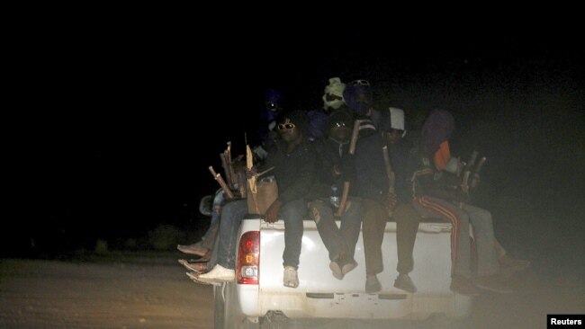 FILE - Migrants sit at the back of a truck as it is driven through a dust road at night in the desert town of Agadez, Niger, May 25, 2015.