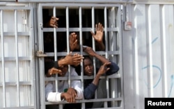 FILE - Illegal migrants, who have been detained after trying to get to Europe, look out of barred door of a detention hut at a detention camp in Gheryan, outside Tripoli, Libya.