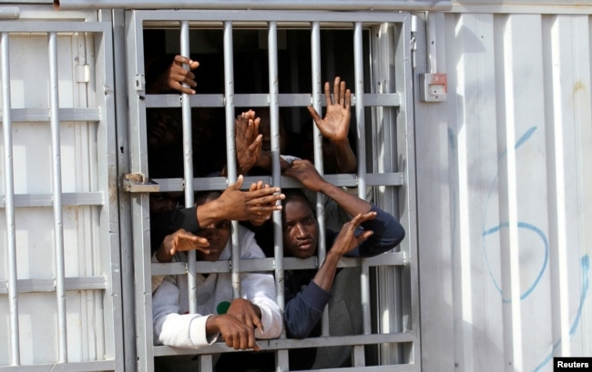 FILE - Illegal migrants, who have been detained after trying to get to Europe, look out of barred door of a detention hut at a detention camp in Gheryan, outside Tripoli, Libya.