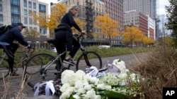 A bicyclist passes bouquets of flowers left by Argentine President Mauricio Macri and New York Mayor Bill de Blasio at the site of the terrorist attack, Nov. 6, 2017. Five Argentine cyclists were among eight people killed, Oct. 31.