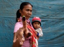 Seorang ibu sambil menggendong bayinya menunjukkan jarinya usai mencoblos di Bondowoso, Jawa Timur dalam pemilu 2014 (Foto Reuters/Sigit Pamungkas).