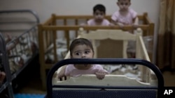 FILE - In this Aug. 15, 2018 file, photo, baby girls stand up in their cribs at Salhiya Orphanage, which now hosts foreign and Iraqi children of IS militants, in Baghdad, Iraq.