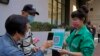 FILE - A staff holding the government's contact tracing QR code for the 'LeaveHomeSafe' COVID-19 mobile app as people line up to receive China's Sinovac COVID-19 coronavirus vaccine at a community vaccination center in Hong Kong, Nov. 29, 2021. 