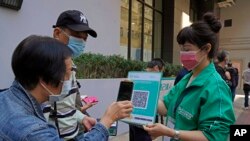 FILE - A staff holding the government's contact tracing QR code for the 'LeaveHomeSafe' COVID-19 mobile app as people line up to receive China's Sinovac COVID-19 coronavirus vaccine at a community vaccination center in Hong Kong, Nov. 29, 2021. 