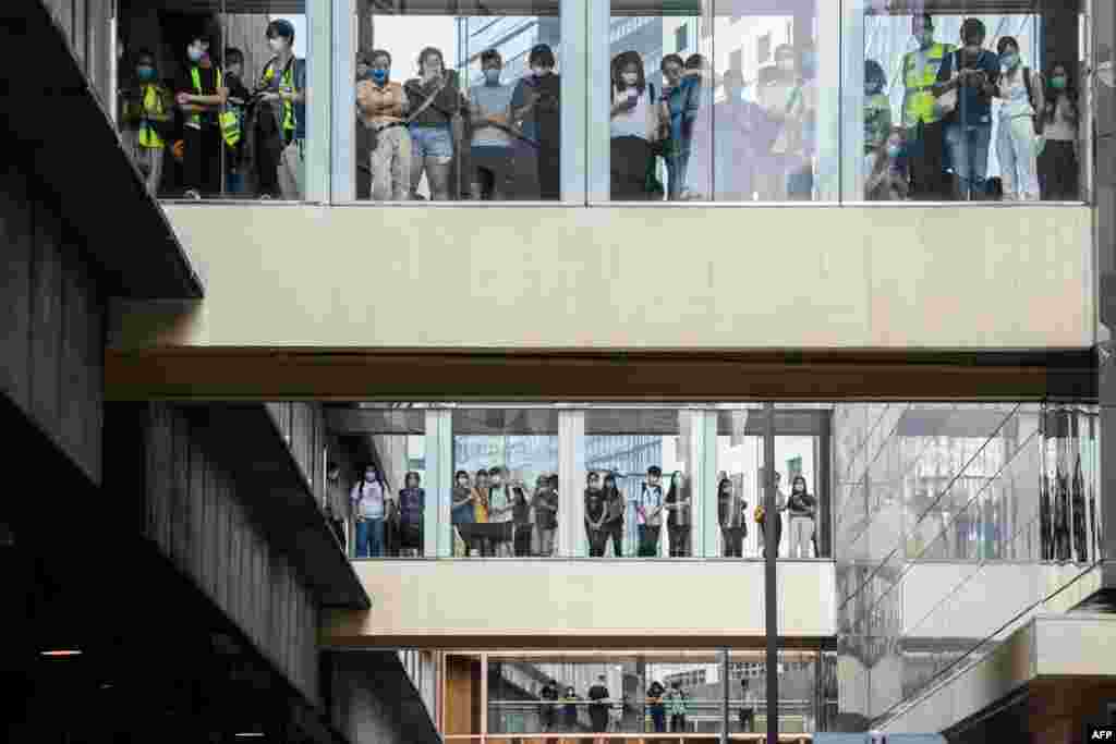Bystanders watch from footbridges as riot police (not seen) stand guard outside a building below in Hong Kong, as the city&#39;s legislature debates a law that bans insulting China&#39;s national anthem.