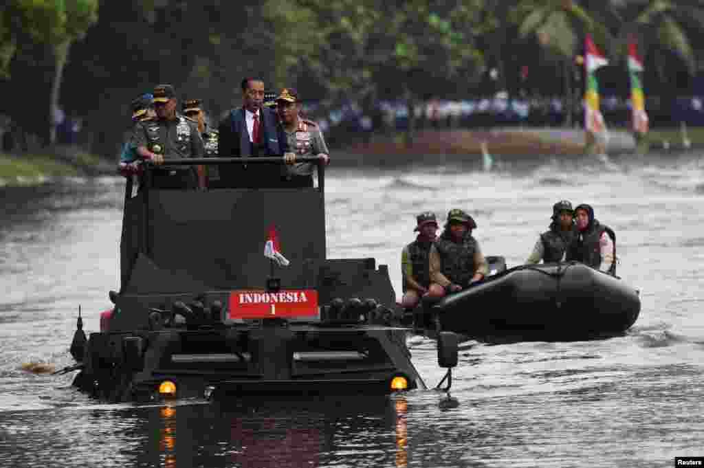 (L-R) Indonesian Military Chief Gatot Nurmantyo, President Joko Widodo, and Police Chief Tito Karnavian stand on a military amphibious vehicle Anoa 2 while crossing a lake in Jakarta, in this photo taken by Antara Foto.