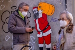 Warga mengenakan masker FFP2 di tengah pandemi COVID-19 di depan mural yang menggambarkan Sinterklas, di Madrid, Spanyol, 12 Januari 2022.
