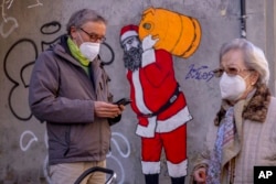 People wear FFP2 masks amid the COVID-19 pandemic in front of a mural depicting Santa Claus in Madrid, Spain, January 12, 2022.