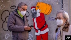 A man and woman wearing FFP2 masks to curb the spread of COVID-19 are seen in front of a mural depicting Santa Claus, in Madrid, Spain, Jan. 12, 2022.