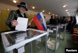 FILE - A woman holds a Russian flag as she casts her ballot during the referendum on the status of Ukraine's Crimea region at a polling station in Bakhchisaray March 16, 2014.