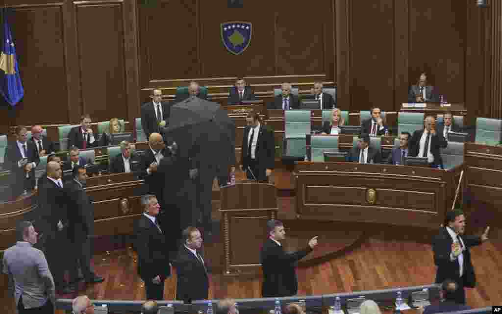 Bodyguards escort Kosovo&#39;s Prime Minister Isa Mustafa, covering with an umbrella, away from the stand as opposition members hurl eggs while he is addressing parliament in capital Pristina, on the latest agreement reached between Kosovo and Serbia.