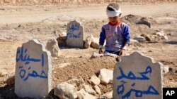 一名8歲大的伊拉克兒童坐在他母親和姊姊的墳墓前。他的家人在10月的一次汽車炸彈爆炸襲擊中死亡。