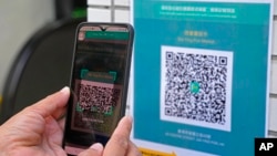FILE - A woman scans the government's contact-tracing QR code for the LeaveHomeSafe COVID-19 mobile app before entering a market in Hong Kong, Nov. 2, 2021. 