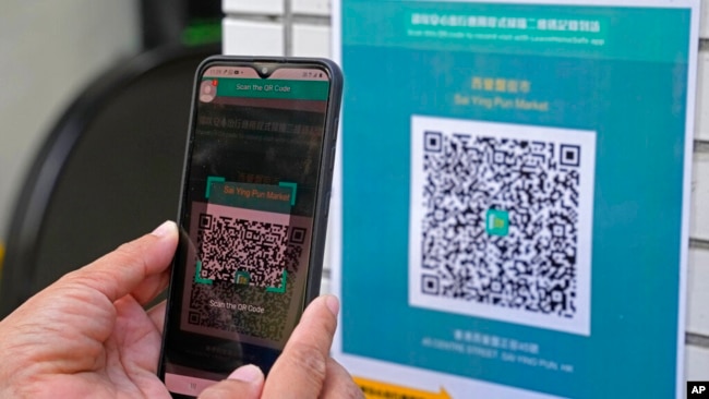 FILE - A woman scans the government's contact-tracing QR code for the LeaveHomeSafe COVID-19 mobile app before entering a market in Hong Kong, Nov. 2, 2021.