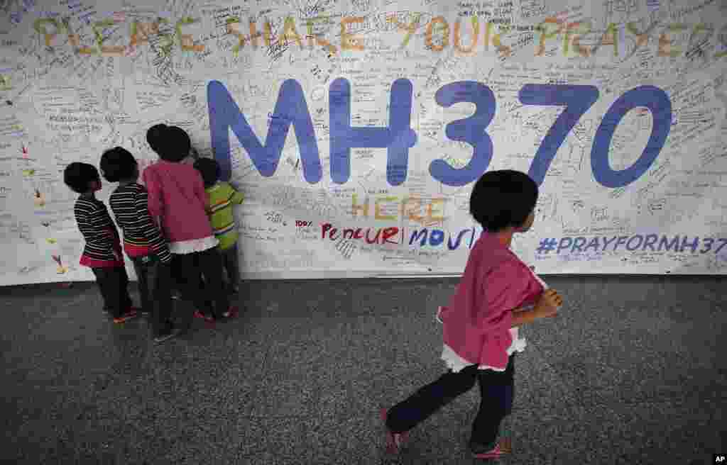 3月13日在吉隆坡国际机场，孩子们读着贴在墙上为所有卷入马航失联航班事件的人留下的表达良好愿望的留言