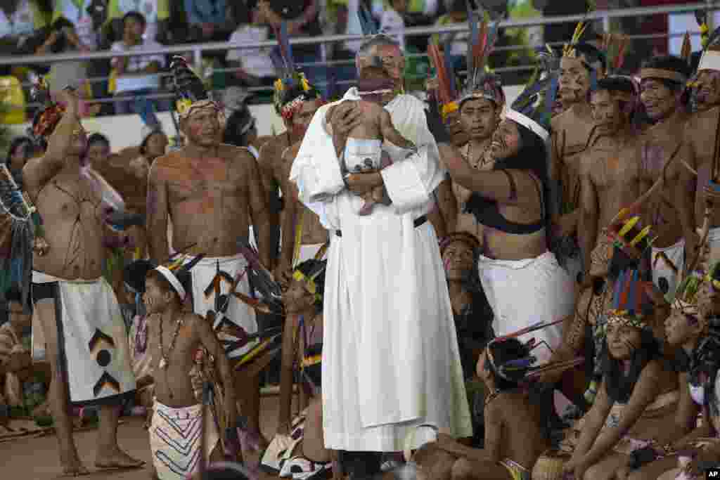 A priest holds a baby as clergy and indigenous people wait for the arrival of Pope Francis in Puerto Maldonado, Madre de Dios province, Peru.
