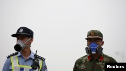 A paramilitary policeman and a policeman, both wearing masks, stand guard at a location within a 3-km (2-mile) exclusion zone from last week's explosion site in Binhai new district in Tianjin, China, Aug. 18, 2015. 