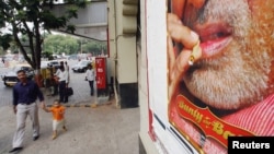 FILE - A man and child walk past a billboard showing Bollywood star Bachchan smoking in one of his films, in Bombay, India.