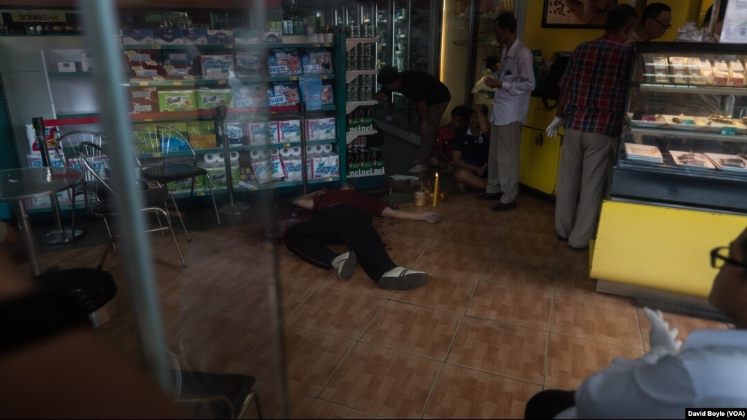 FILE - Police survey the crime scene where Kem Ley was shot dead while family members pray next to his dead body, July 10, 2016.