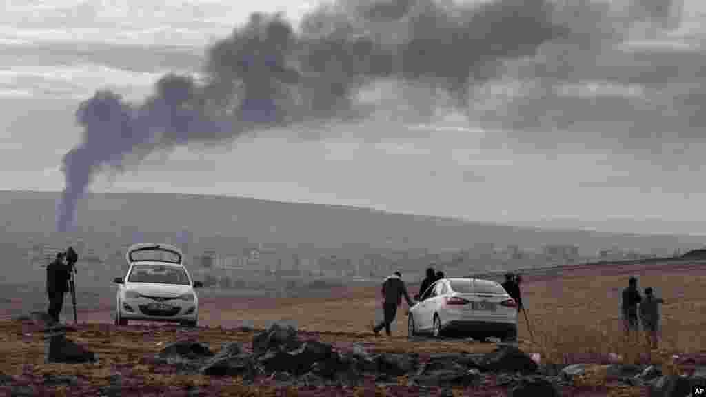 Members of the media on a hilltop on the outskirts of Suruc, at the Turkey-Syria border, watch as smoke from a fire rises following a strike in Kobani, Syria, during fighting between Syrian Kurds and the militants of Islamic State group, Oct. 19, 2014. 