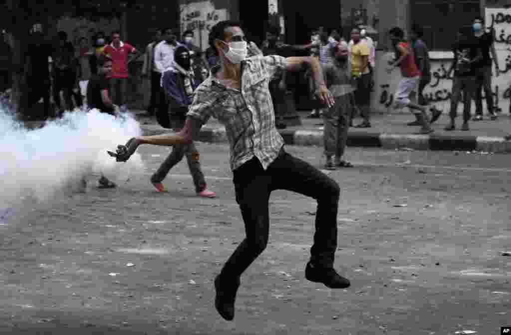  یک معترض مصری یک گاز اشک آور بسوی پلیس ضد شورش در خارج از سفارت&nbsp;&nbsp; امریکا پرتاب می کند.