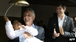 FILE - A handout picture released by Argentina's Presidency shows Argentine President Mauricio Macri holding a school girl while she rings a bell next to then Education Minister Esteban Bullrich during an official ceremony to launch the school year in Vol