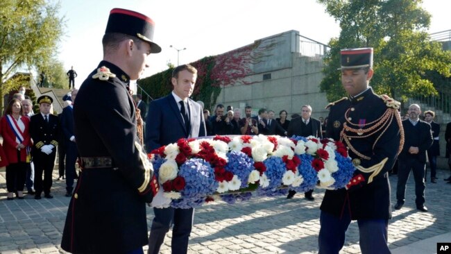 French President Emmanuel Macron, center, lays a wreath near the Pont de de Bezons, where the 1961 protest started, Oct. 16, 2021, in Colombes near Paris.