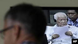 A journalist listens to Khieu Samphan, center, former Khmer Rouge head of state, as he appears on TV screen at the court press center of the U.N.-backed war crimes tribunal in Phnom Penh, Wednesday, Nov. 23, 2011. The trial for three top Khmer Rouge leade