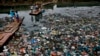 FILE - A man guides a raft through a polluted canal littered with plastic bags and other garbage in Mumbai, India, Oct. 2, 2016.