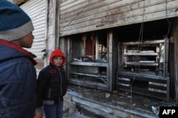 FILE - Syrian boys look at the destroyed grills outside a shuttered restaurant that was the site of a suicide attack targeting U.S.-led coalition forces in Manbij, Syria, the previous day, on Jan. 17, 2019. Islamic State claimed responsibility for the attack.