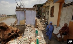 FILE - A woman walks past a partly demolished houses ahead of an eviction by the government in Jakarta, Indonesia, Sept. 20, 2016.