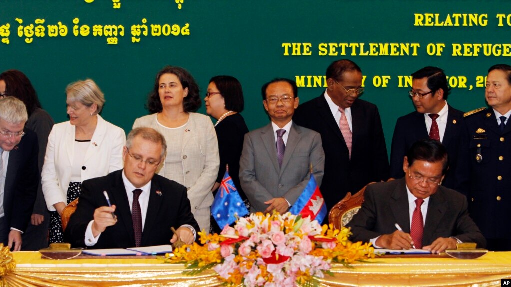 FILE - Australian Immigration Minister Scott Morrison, front left, signs a document together with Cambodian Interior Minister Sar Kheng, front right, during a signing ceremony of a controversial deal on resettlement of refugees inside the Interior Ministry in Phnom Penh, Cambodia, Friday, Sept. 26, 2014. 