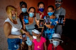 Zuleydis "Zuly" Elledias, left, shows a cellphone photo of her missing husband to a child while her neighbors pose for a group picture holding up cellphone photos of their missing relatives who ventured out in homemade boats in an attempt to reach Florida