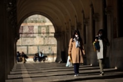 Tourists wearing protective masks walk along an arcade at the St. Mark's Square in Venice, Italy, Friday, Feb. 28, 2020. Authorities in Italy decided to re-open schools and museums in some of the areas less hard-hit by the coronavirus.