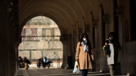Tourists wearing protective masks walk along an arcade at the St. Mark's Square in Venice, Italy, Friday, Feb. 28, 2020. Authorities in Italy decided to re-open schools and museums in some of the areas less hard-hit by the coronavirus.