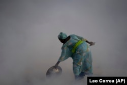 Ndeye Yacine Dieng drops embers over peanut shells covering fish as she walks amidst the smoke on Bargny beach, some 35 kilometers (22 miles) east of Dakar, Senegal, Wednesday April 21, 2021.