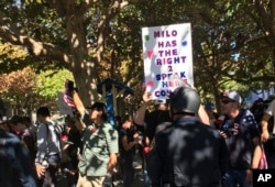 FILE - Berkeley police officers stand guard for planned speech by Milo Yiannopoulos in Berkeley, Calif., Sept. 24, 2017. Milo Yiannopoulos was whisked away in a car after a brief appearance at the school that drew a few dozen supporters and a slightly larger crowd of protesters.