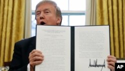 President Donald Trump holds up one of the Section 201 actions that he signed during a ceremony in the Oval Office of the White House in Washington, Jan. 23, 2018. Trump says he is imposing new tariffs to "protect American jobs and American workers." 