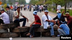 FILE - Rubber farmers sit on tires as they block a road during a protest in Surat Thani, Sept. 3, 2013. 