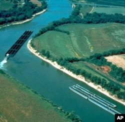 A long barge, full of coal and pushed by a tug, makes the tricky turn around one of the bends in the Cumberland River in Kentucky.