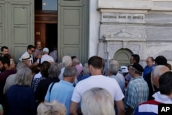 FILE - The first customers, most of them pensioners, stand in a queue to enter a branch at National Bank of Greece headquarters in Athens, Monday, July 20, 2015.
